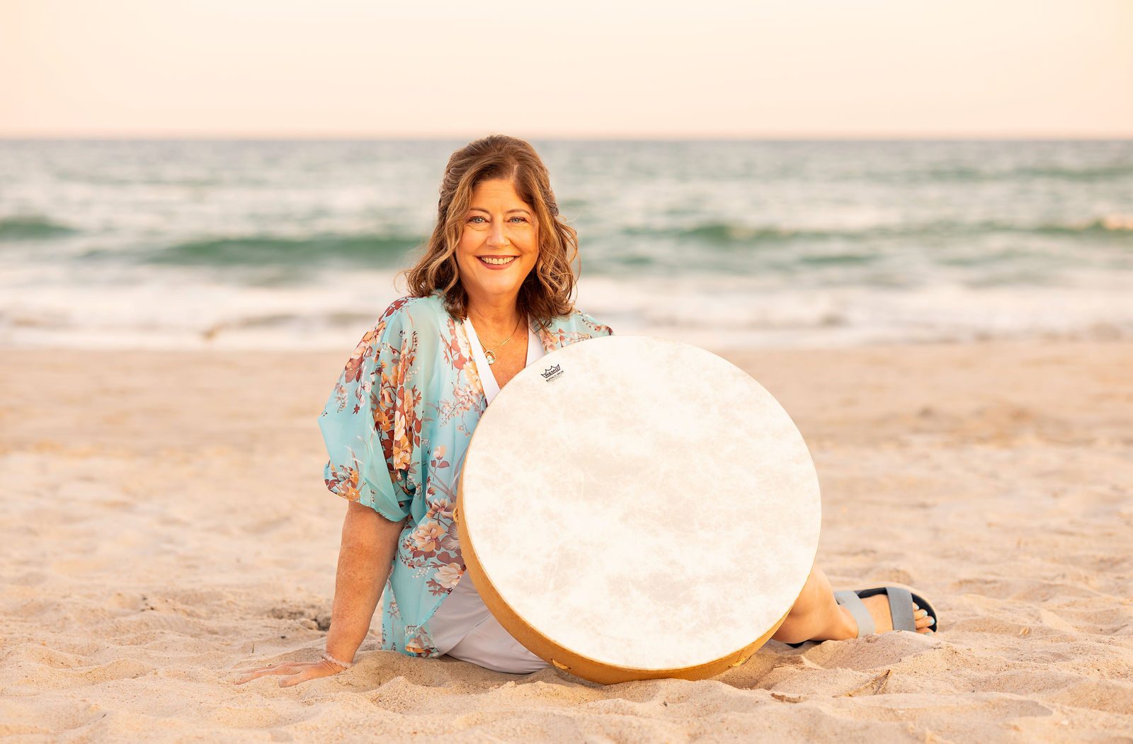 Melinda Cornish sitting on the sand with her frame drum at sunset